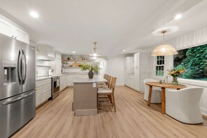 Een moderne keuken met een centraal eiland, roestvrijstalen apparatuur en een eethoek met een ronde houten tafel en stoelen.