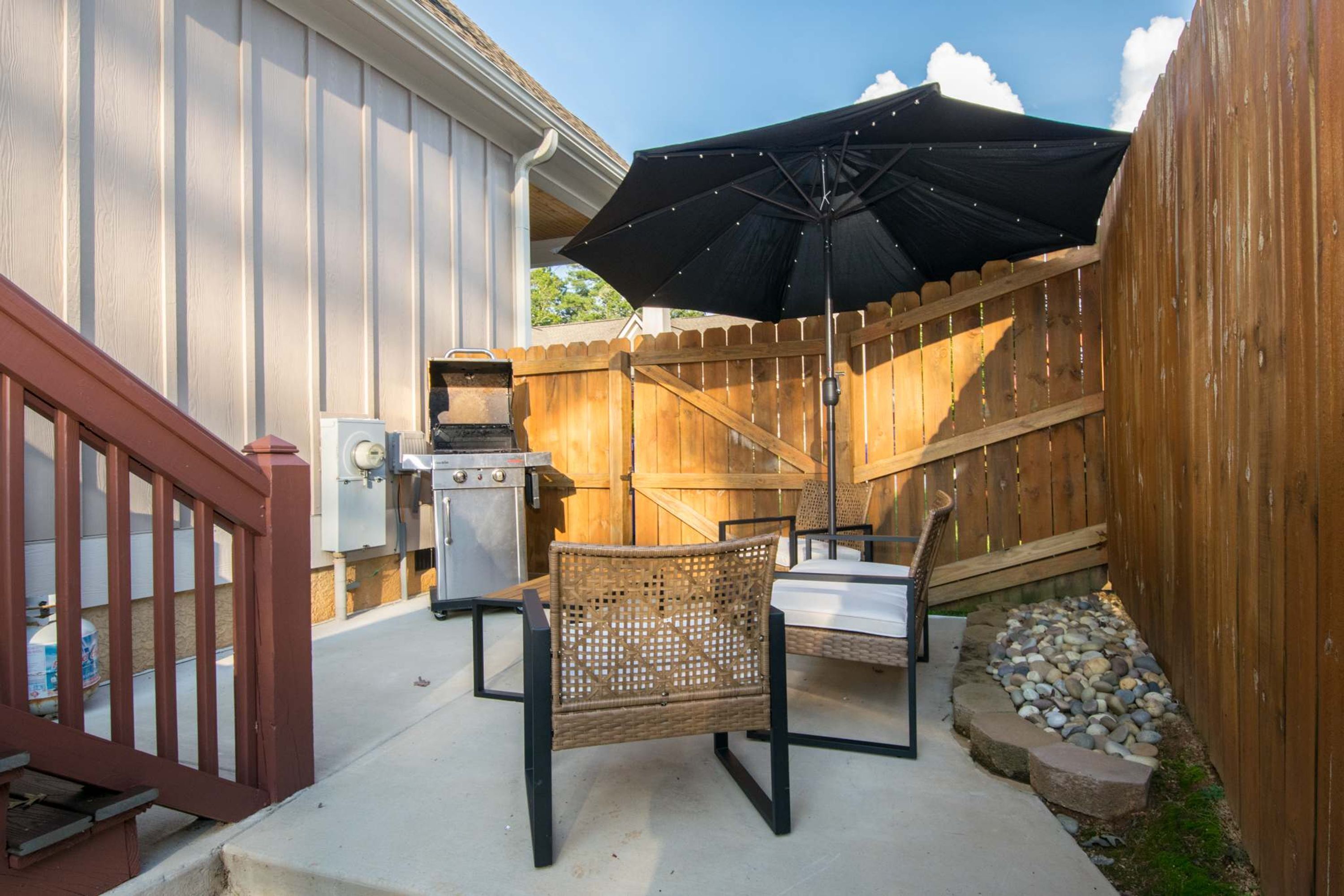 An outdoor patio area with a grill, chairs, and a large umbrella.
