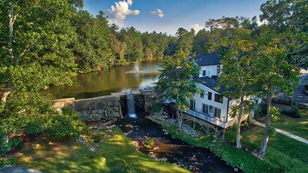 Une maison avec un étang, une cascade et une végétation luxuriante.