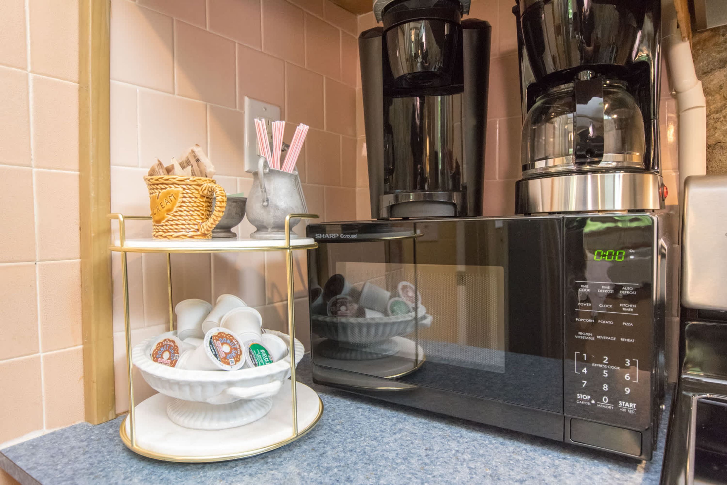 A kitchen with a microwave, coffee maker, and a shelf with cups and a basket.