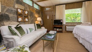Une pièce chaleureuse avec un mur en pierre, un canapé blanc, un lit, une télévision et une fenêtre avec des rideaux.