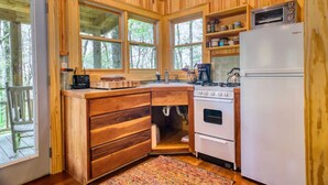 A wooden cabin kitchen with a stove, oven, refrigerator, and a coffee maker. - Cozy Guest Cabin Pet Friendly Secluded Peaceful (Chimney Rock)