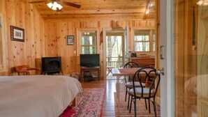 A wooden cabin interior with a bed, a television, a dining table, and chairs. - Cozy Guest Cabin Pet Friendly Secluded Peaceful (Chimney Rock)