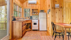 A wooden cabin with a kitchen featuring a stove, oven, and refrigerator, a dining area with chairs, and large windows. - Cozy Guest Cabin Pet Friendly Secluded Peaceful (Chimney Rock)
