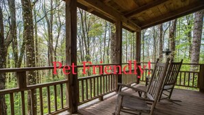 A wooden deck with a railing, surrounded by trees, and two rocking chairs. - Cozy Guest Cabin Pet Friendly Secluded Peaceful (Chimney Rock)