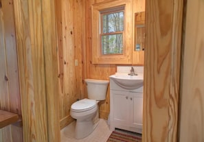 A wooden-paneled bathroom with a toilet, sink, and window. - Cozy Guest Cabin Pet Friendly Secluded Peaceful (Chimney Rock)
