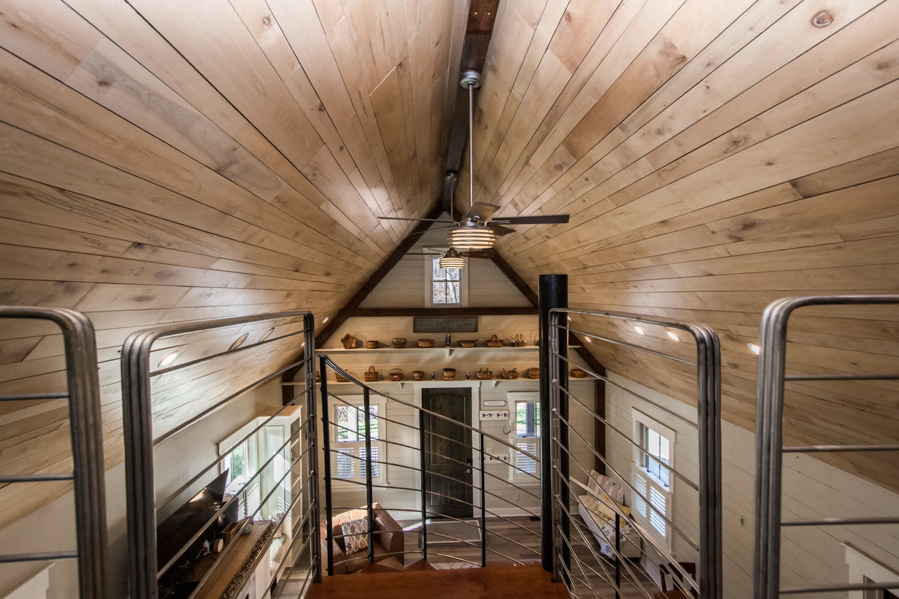 A wooden interior with a staircase, metal railings, and a ceiling fan.