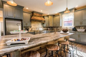 A modern kitchen with grey cabinets, a large island with stools, and a farmhouse-style stove. - Rustic-chic 2BR Cabin w Clawfoot Tub Near Trails (Hendersonville)