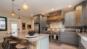 A modern kitchen with a central island, bar stools, and a large stove. - Rustic-chic 2BR Cabin w Clawfoot Tub Near Trails (Hendersonville)