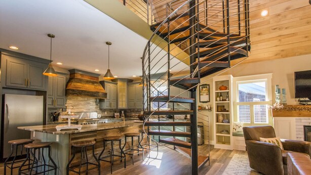 A modern kitchen with a central island, bar stools, a spiral staircase, and a cozy seating area with a fireplace. - Rustic-chic 2BR Cabin w Clawfoot Tub Near Trails (Hendersonville)