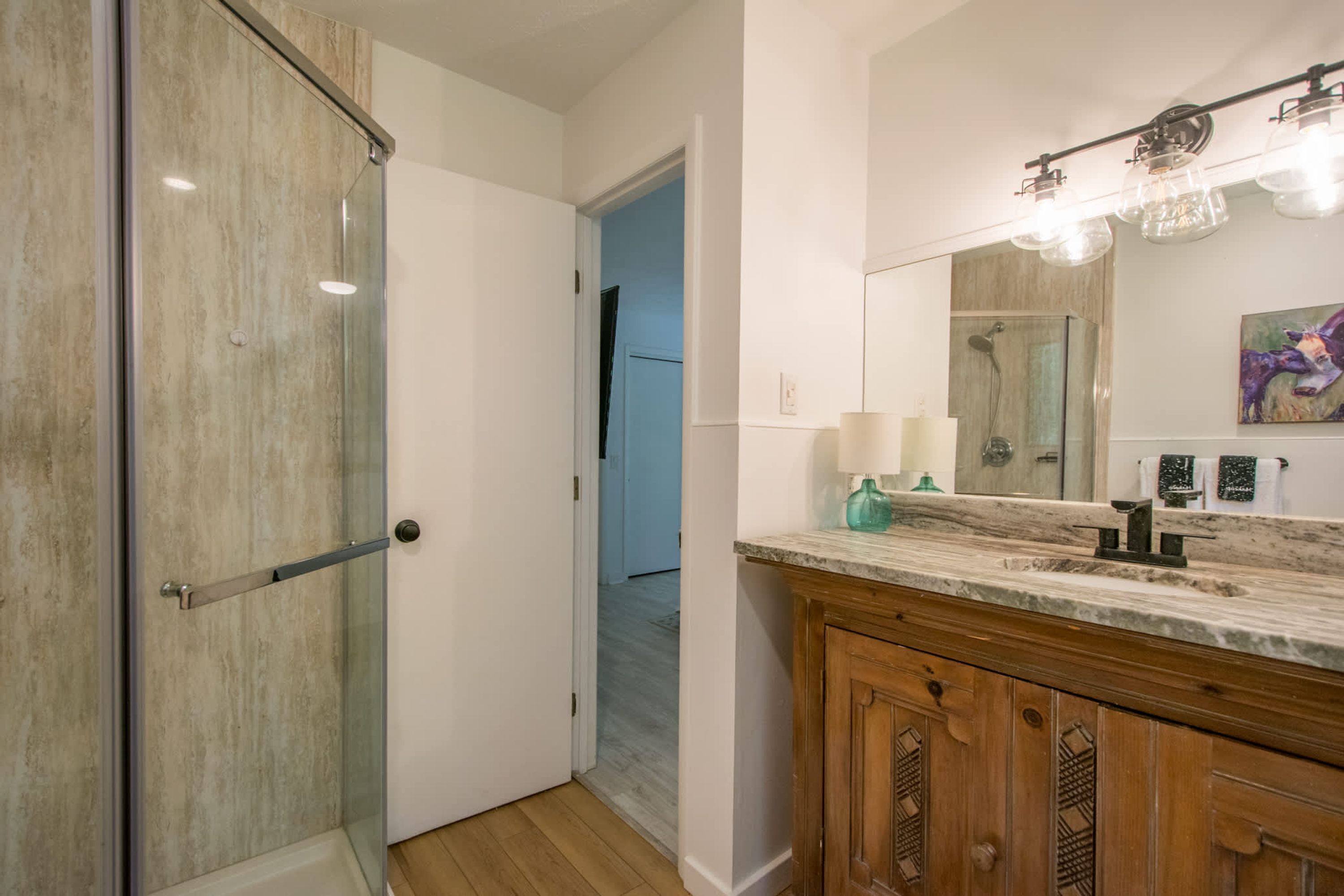 Une salle de bain moderne avec une porte de douche en verre, un meuble-lavabo en bois et un grand miroir avec éclairage intégré.