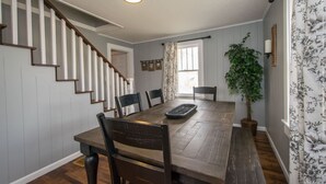 A dining area with a wooden table, chairs, a plant, and a staircase. - Cozy 3BR w Free Attraction Tix 6 Mins to Town (East Flat Rock)