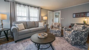 A living room with a grey sofa, a patterned armchair, a round coffee table, and a lamp on a side table. - Cozy 3BR w Free Attraction Tix 6 Mins to Town (East Flat Rock)