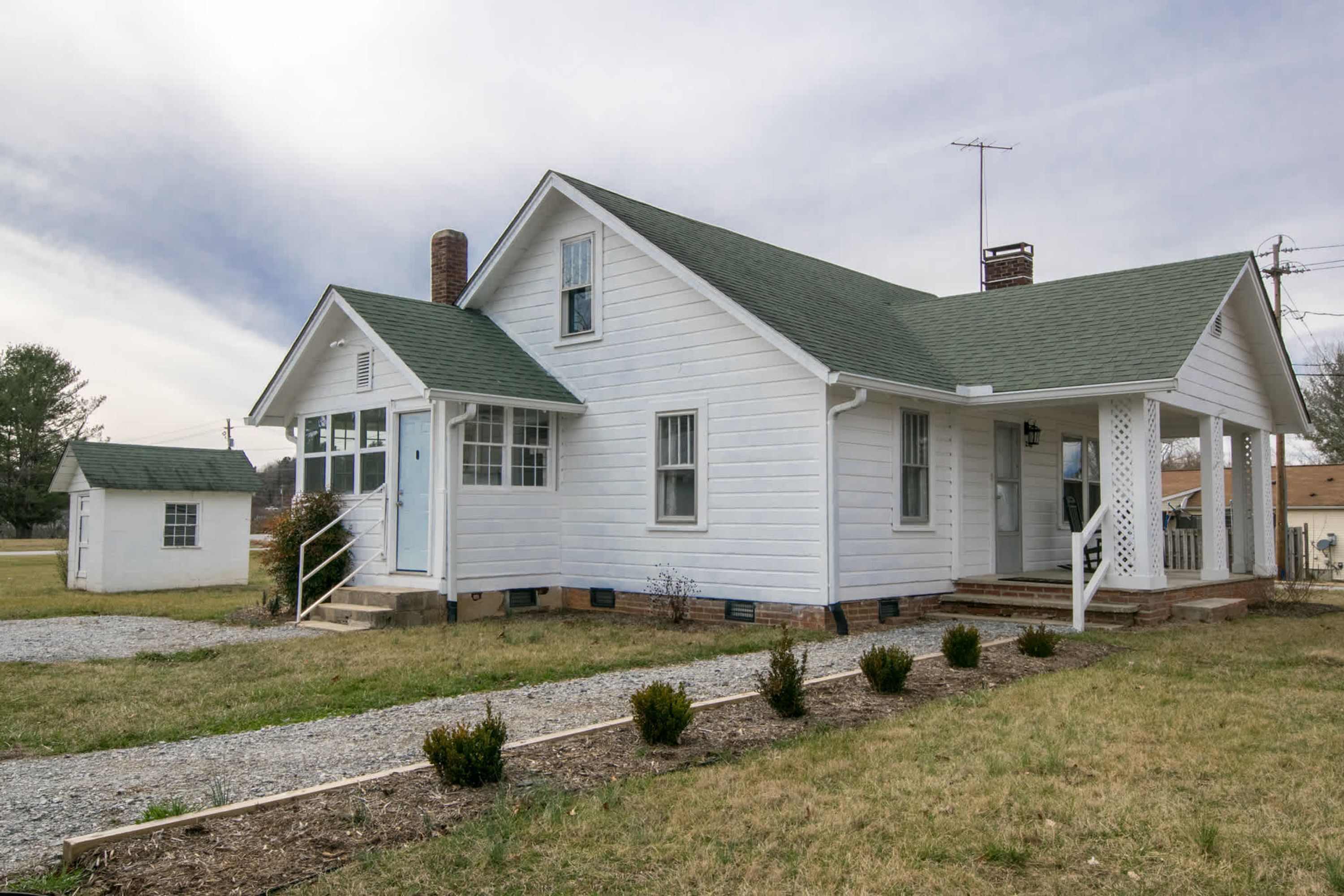 A white two-story house with a green roof, a porch, and a small attached garage.