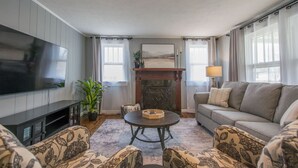 A living room with a flat-screen TV, a fireplace, a sofa, and patterned armchairs. - Cozy 3BR w Free Attraction Tix 6 Mins to Town (East Flat Rock)