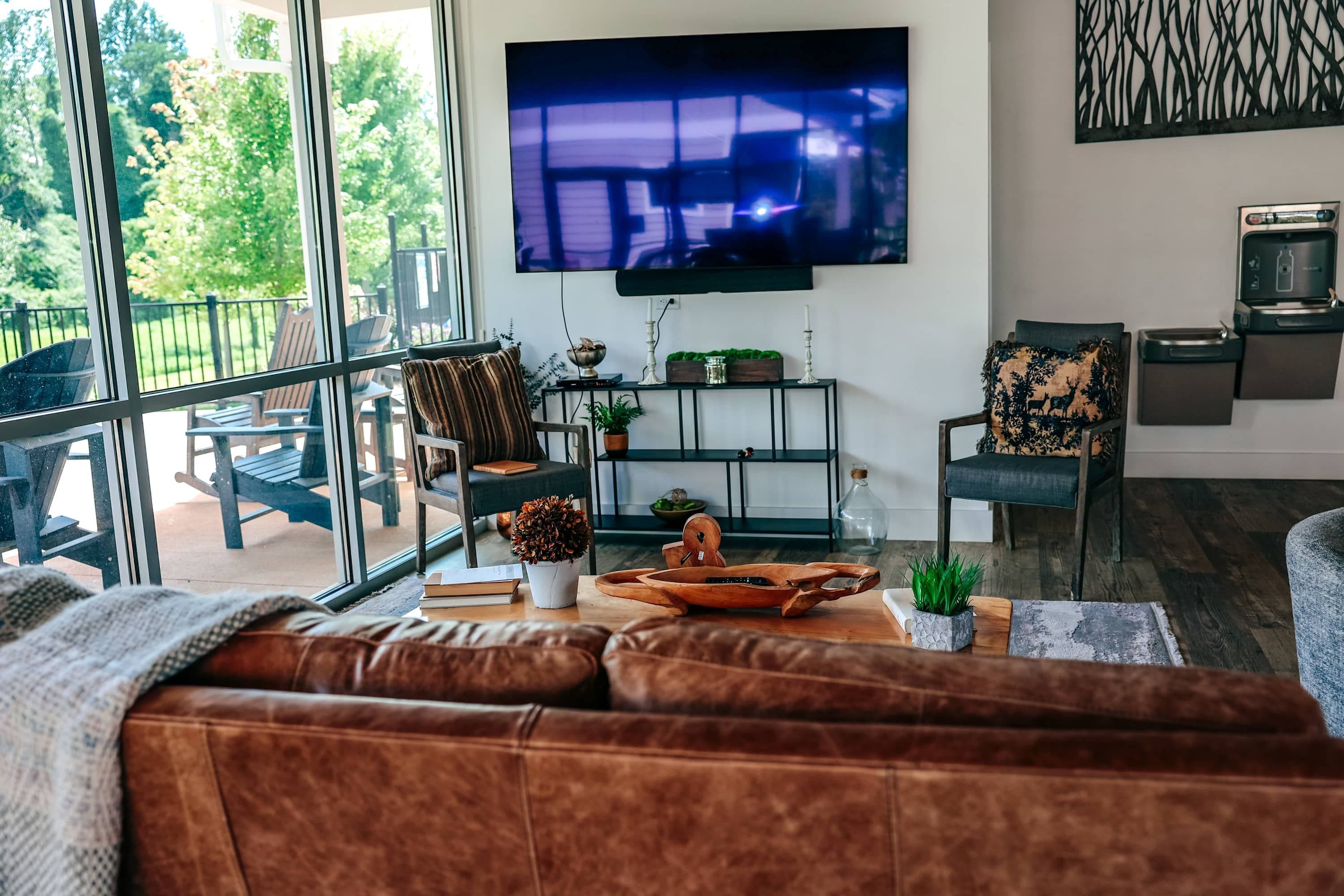 A modern living room with a large TV, comfortable seating, and a view of the outdoors.
