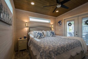 A bedroom with a large bed, wooden walls, a ceiling fan, a nightstand, and a window. - 1BR Tiny Home w King Bed Outdoor Space (Flat Rock)