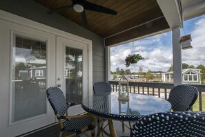 A covered porch with a glass table and wicker chairs, overlooking a residential area. - 1BR Tiny Home w King Bed Outdoor Space (Flat Rock)