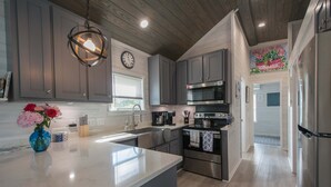 A modern kitchen with grey cabinets, stainless steel appliances, a large island, and a decorative vase with flowers. - 1BR Tiny Home w King Bed Outdoor Space (Flat Rock)