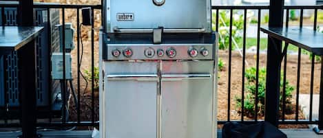 Un barbecue à gaz Weber Summit doté de quatre brûleurs et d’un brûleur latéral, installé sur une terrasse en bois avec une rambarde noire.