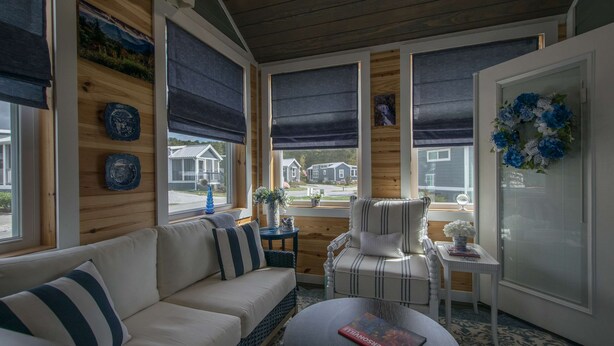 A cozy room with a sofa, chair, and table, featuring wooden walls, large windows with blinds, and a decorative wreath. - 1BR Tiny Home w King Bed Outdoor Space (Flat Rock)