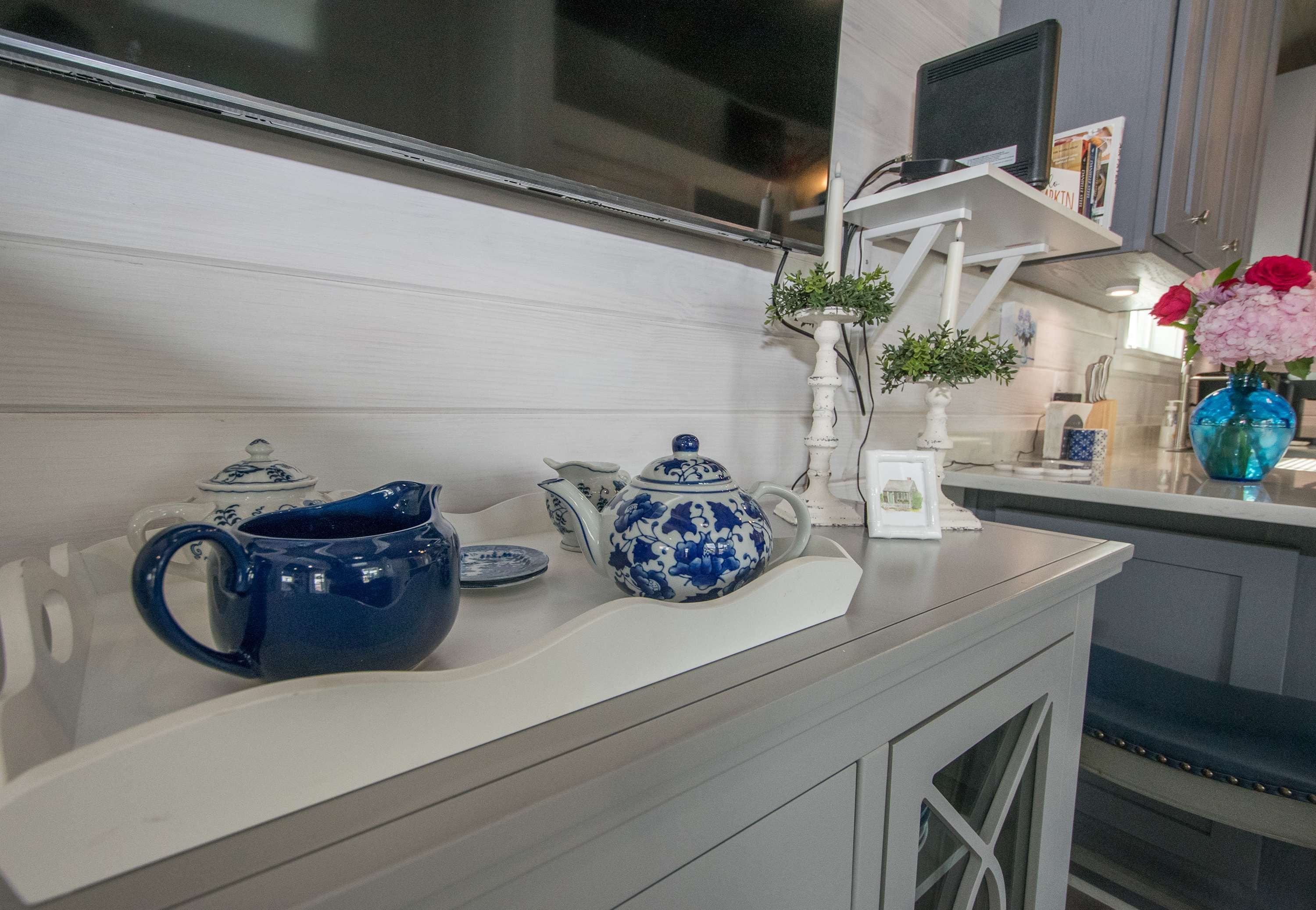 A kitchen counter with a blue teapot, a white teapot, and a blue vase with flowers.