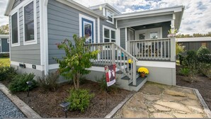 A two-story house with a front porch, a small garden, and a welcome sign. - 1BR Tiny Home w King Bed Outdoor Space (Flat Rock)
