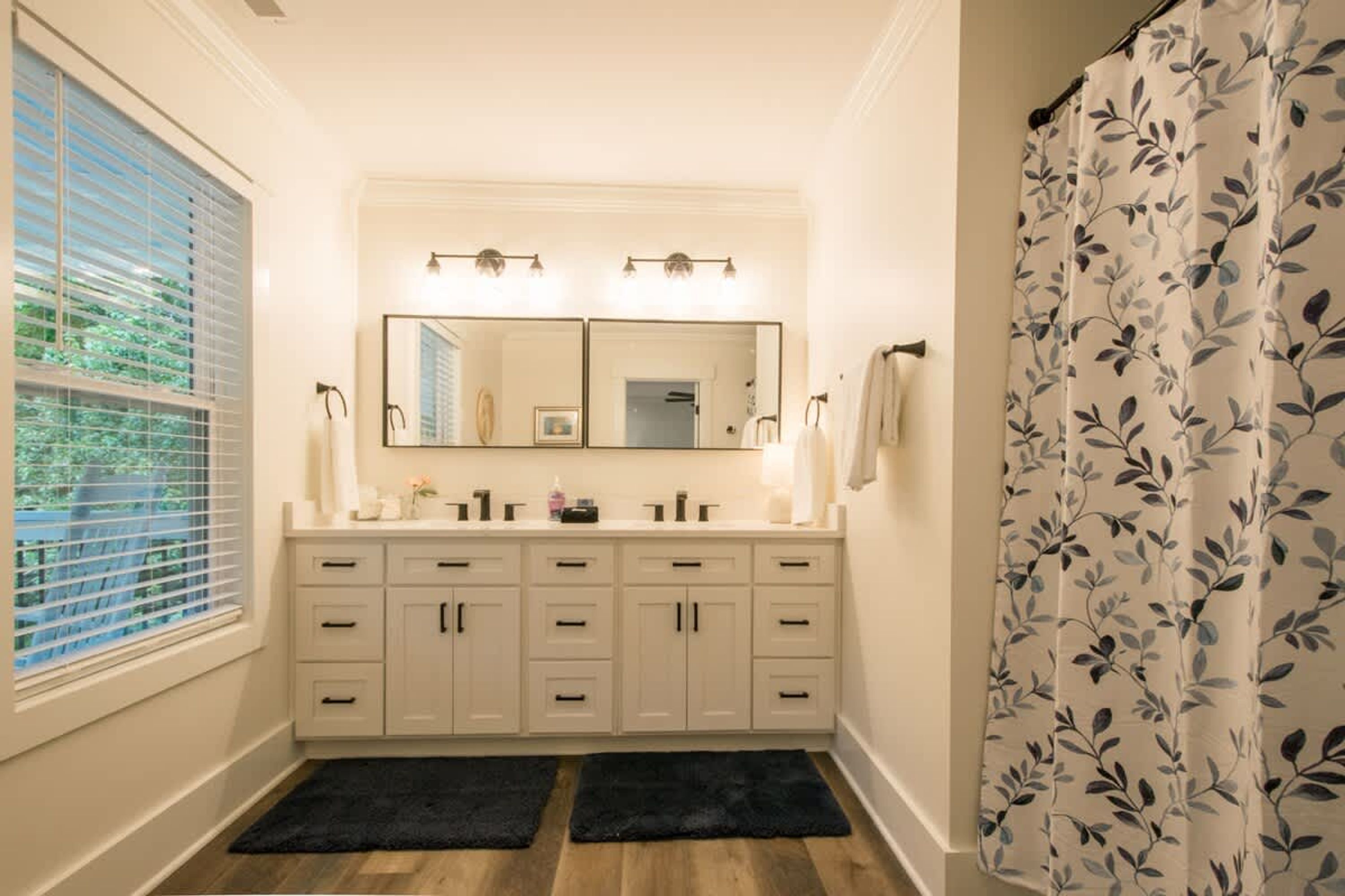 A bathroom with a double vanity, a large mirror, and a shower curtain with a leaf pattern.