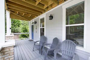 A covered porch with two Adirondack chairs, a wooden ceiling, and a white exterior wall with a blue door and windows. - Charming 3BR w Balconies Walk to Flat Rock Playhouse (Flat Rock)