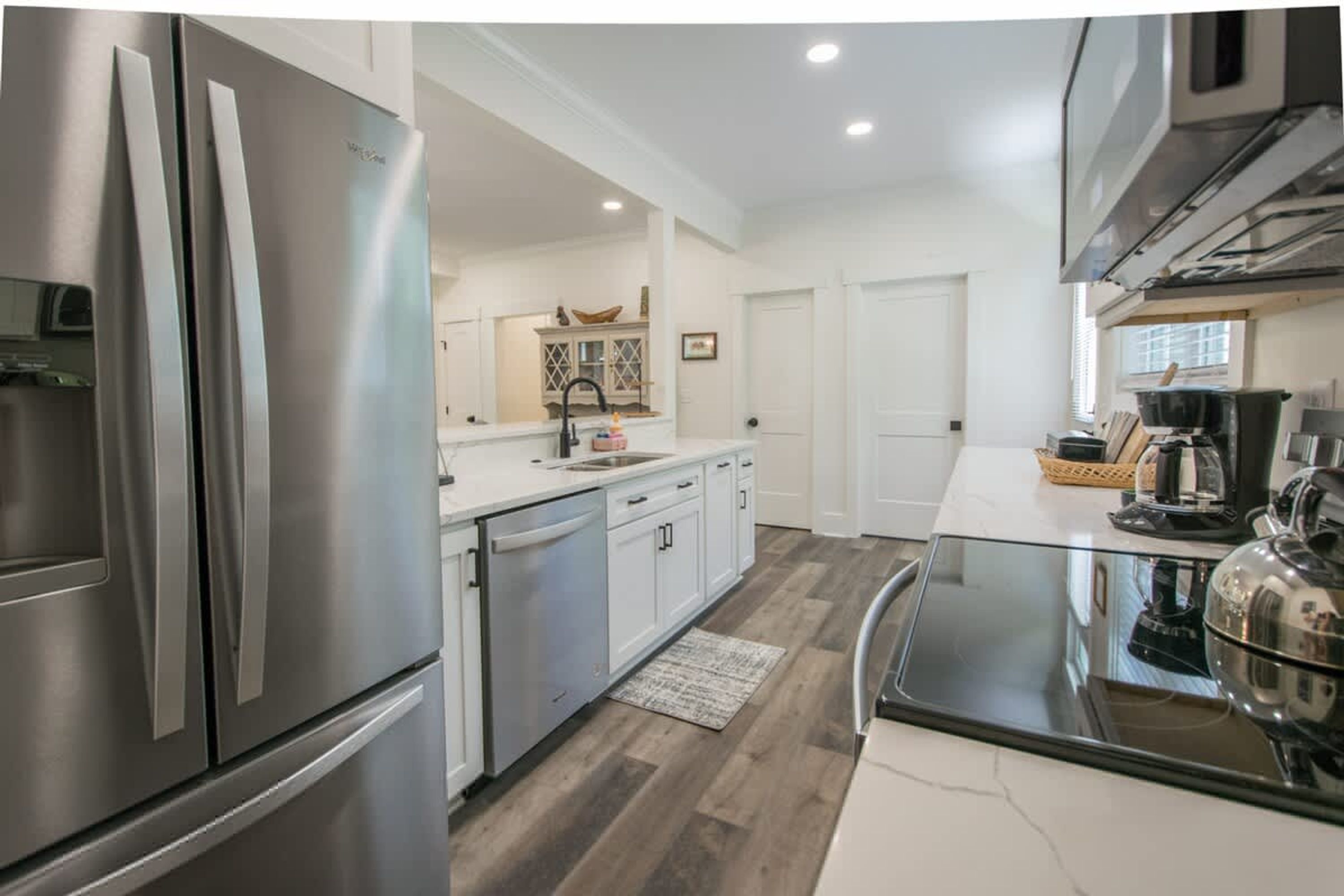 Una cocina moderna con electrodomésticos de acero inoxidable, armarios blancos y suelo de madera.