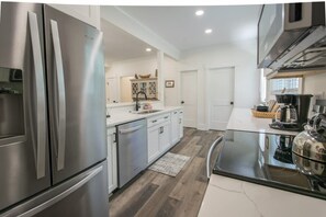 A modern kitchen with stainless steel appliances, white cabinetry, and a wooden floor. - Charming 3BR w Balconies Walk to Flat Rock Playhouse (Flat Rock)
