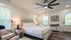 A bedroom with a bed, bedside tables, a chair, a bench, a ceiling fan, and a window with blinds. - Charming 3BR w Balconies Walk to Flat Rock Playhouse (Flat Rock)