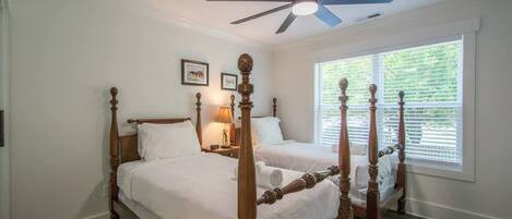 A four-poster bed with a ceiling fan, two bedside tables, and a window with blinds.