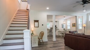 A spacious living area with a staircase, a brown leather sofa, a dining table, and a kitchen in the background. - Charming 3BR w Balconies Walk to Flat Rock Playhouse (Flat Rock)