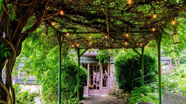 Ein überdachter Gartenweg mit einer Bank und einem Blumentopf, der zu einem Gebäude mit Glastür führt.