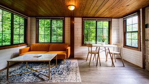 Ein gemütliches Zimmer mit Holzbalkendecke, großen Fenstern, einer Couch, einem Tisch und Stühlen.