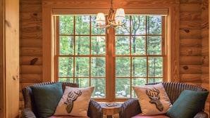 A cozy room with two wicker chairs facing a large window with a view of a forest. - Stylish 3BR Log Cabin w Fire Pit Near Trails (Zirconia)