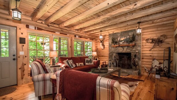 A log cabin interior with a fireplace, wooden furniture, and large windows. - Stylish 3BR Log Cabin w Fire Pit Near Trails (Zirconia)