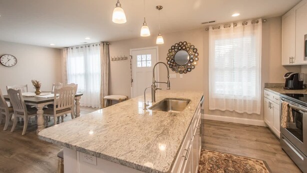 A modern kitchen with a granite countertop, stainless steel appliances, pendant lighting, and a dining area with a table and chairs. - Art-inspired Retreat Free Daily Perks (Asheville)