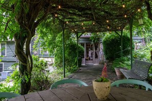 Ein überdachter Außenbereich mit Holztischen und -stühlen, umgeben von üppiger Vegetation und einer Pergola mit Lichterketten.