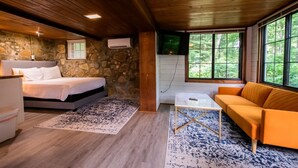 A bedroom with a bed, a nightstand, a stone wall, and a TV mounted on the wall. - Peaceful Woodsy Studio 15 Min to Town Free Tix (Hendersonville)