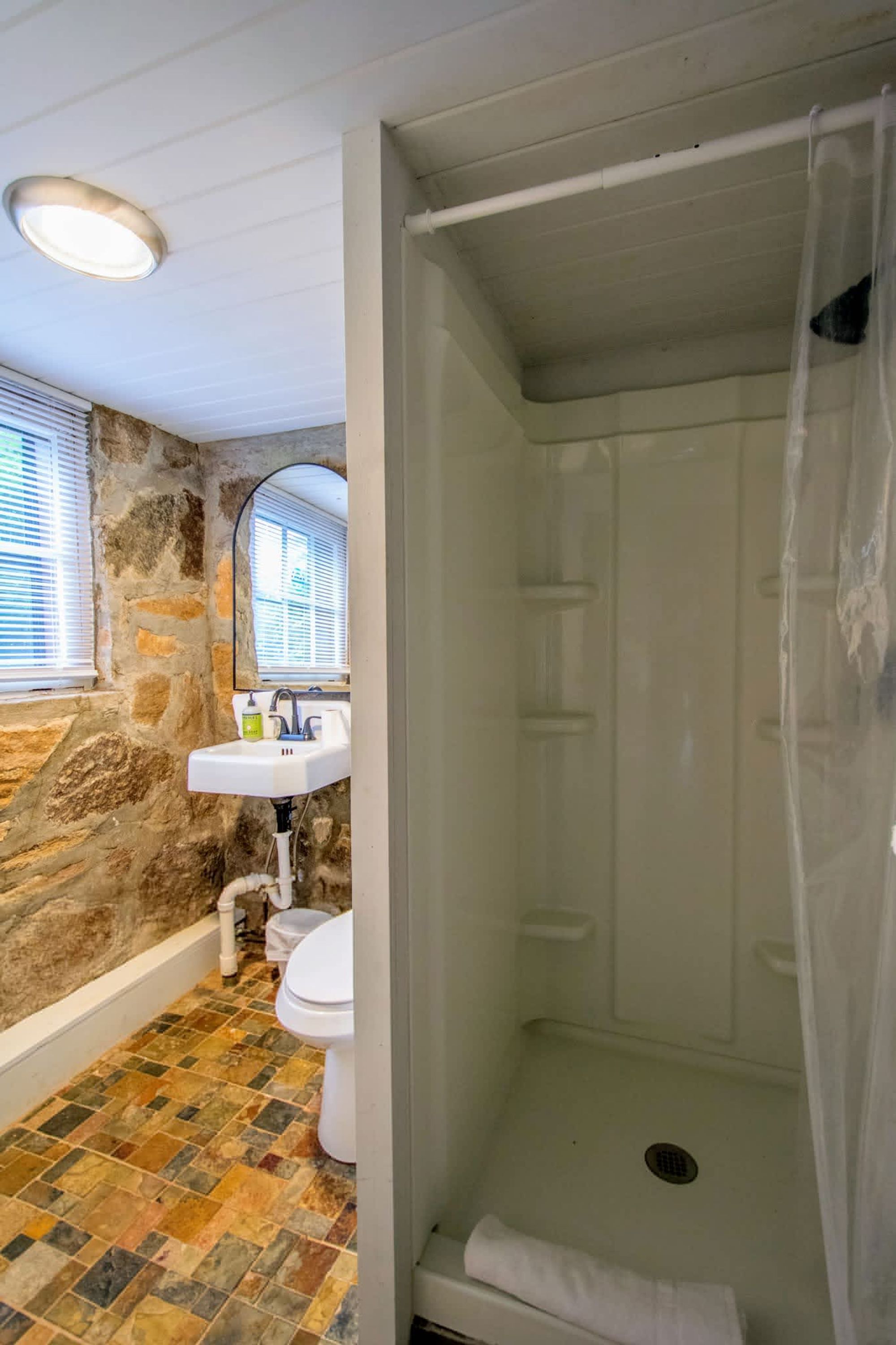 A bathroom with a stone wall, a white sink, a toilet, and a shower with a curtain.