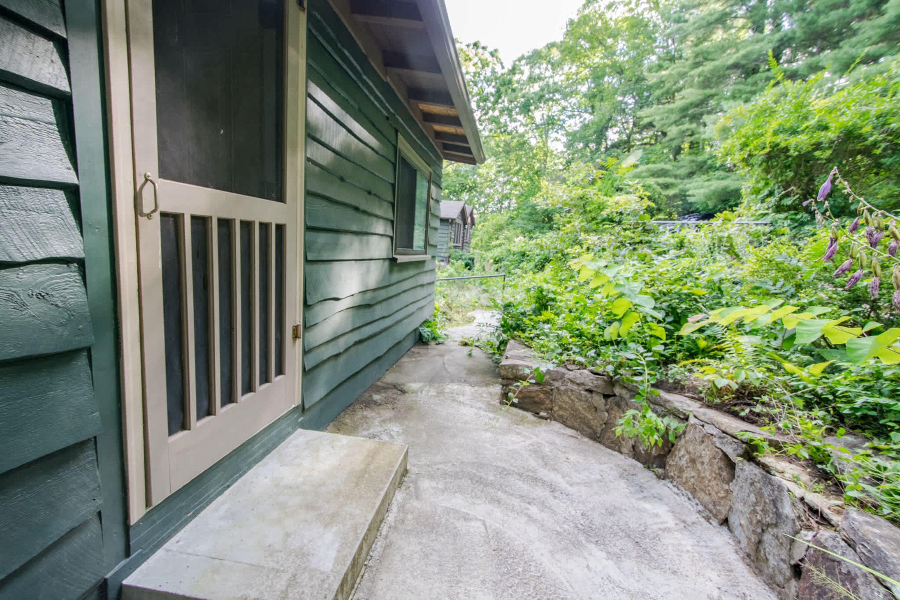 A wooden house with a concrete pathway leading to a door.