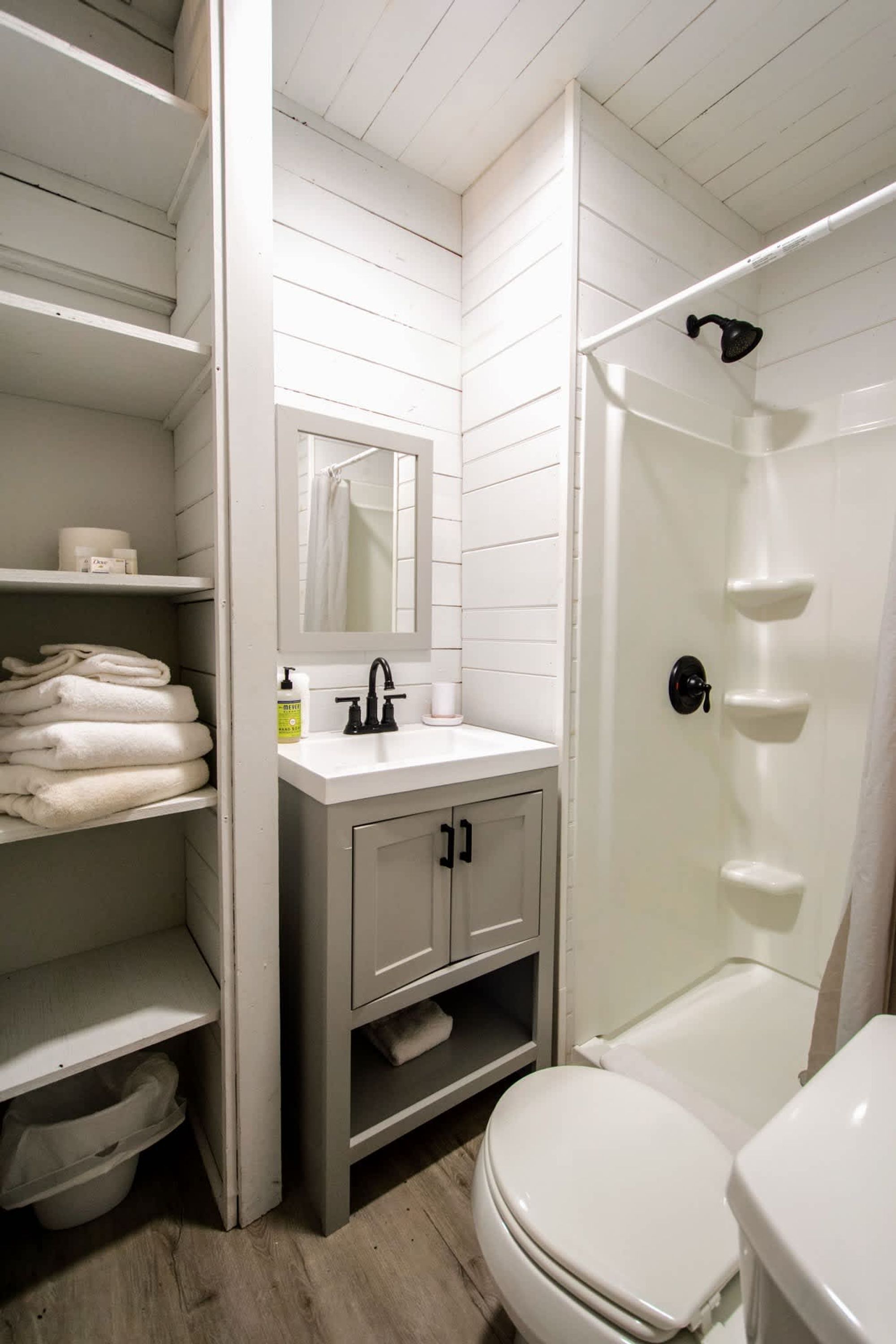 A bathroom with white tiled walls, a white sink, a toilet, and a shower.