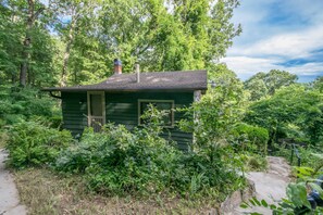 A small, green wooden cabin surrounded by dense greenery and trees. - 1BR Cottage w Patio Free Tix Near Downtown (Hendersonville)