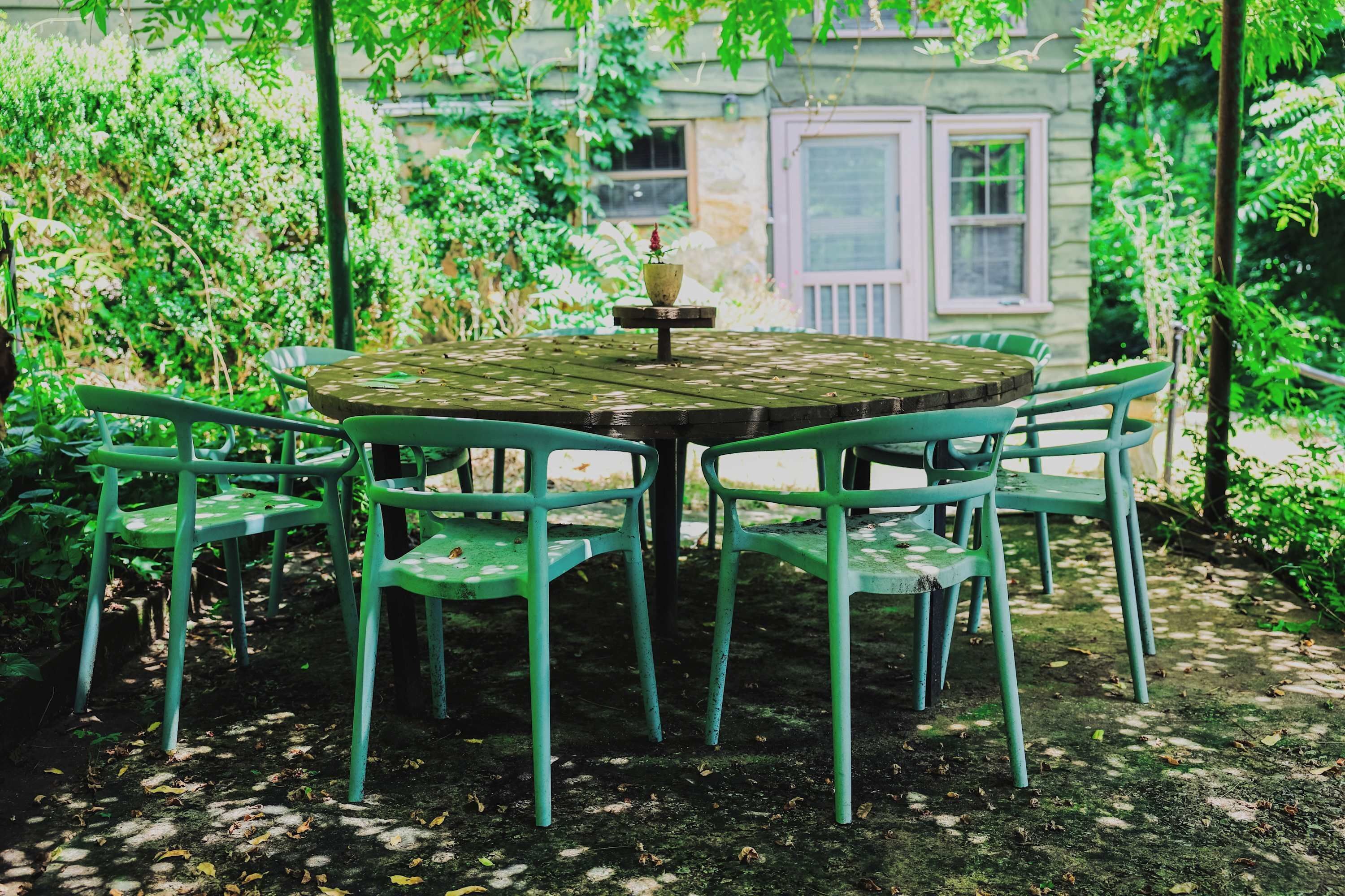 Ein runder Holztisch mit einer Blumenampel in der Mitte, umgeben von sechs grünen Stühlen.