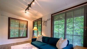 Ein Wohnzimmer mit einem dunkelgrünen Sofa, einem Marmortisch und großen Fenstern mit Jalousien.