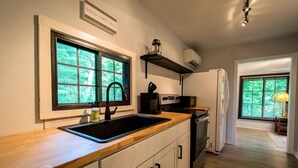 Eine moderne Küche mit Holzarbeitsplatte, einem schwarzen Spülbecken und einem eingebauten Backofen. Ein Fenster bietet Blick auf Grünfläche draußen.