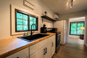 A modern kitchen with a wooden countertop, a black sink, and a built-in oven. There is a window with a view of greenery outside. - 1BR Cottage w Patio Free Tix Near Downtown (Hendersonville)