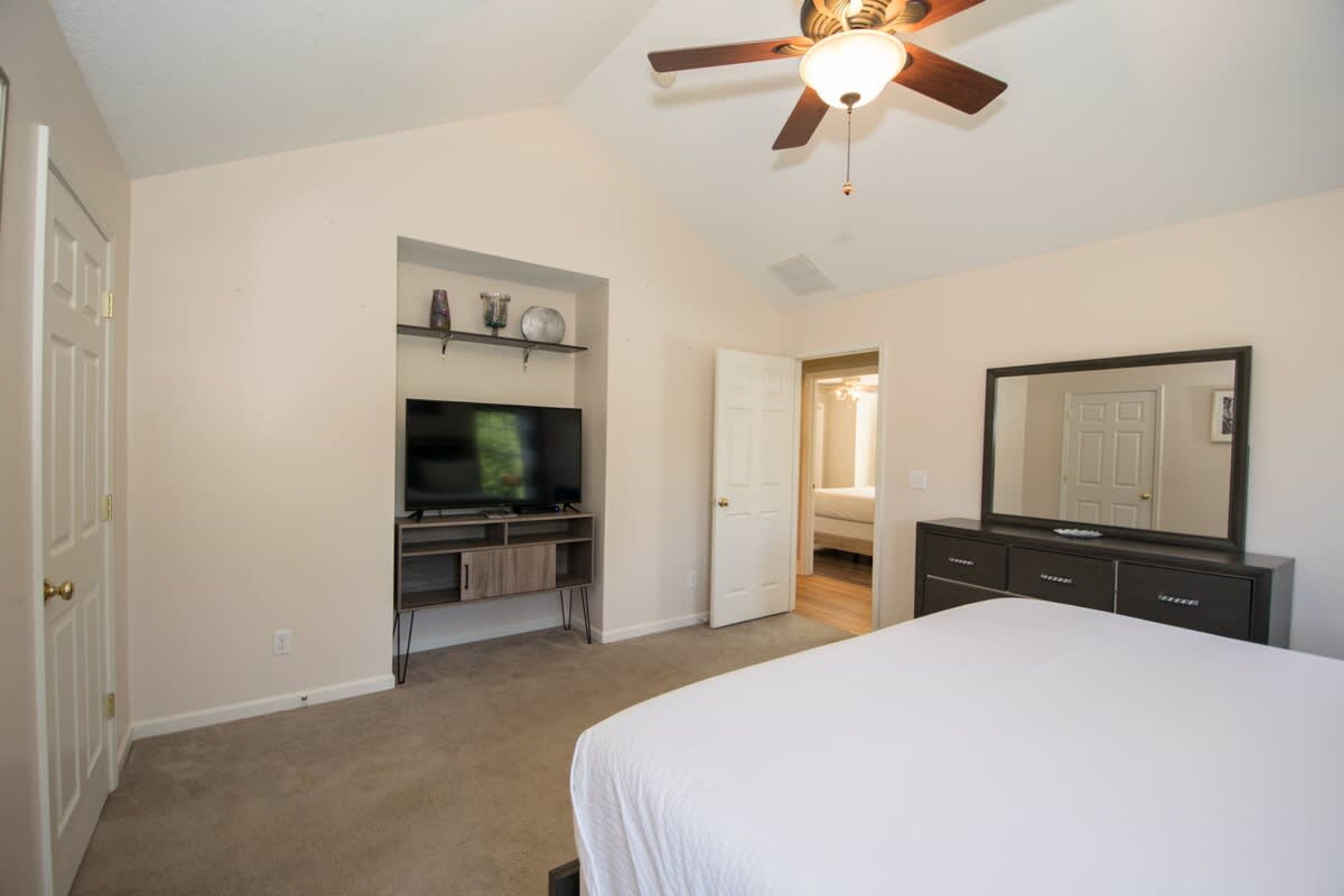 A bedroom with a bed, a TV, a dresser, and a ceiling fan.